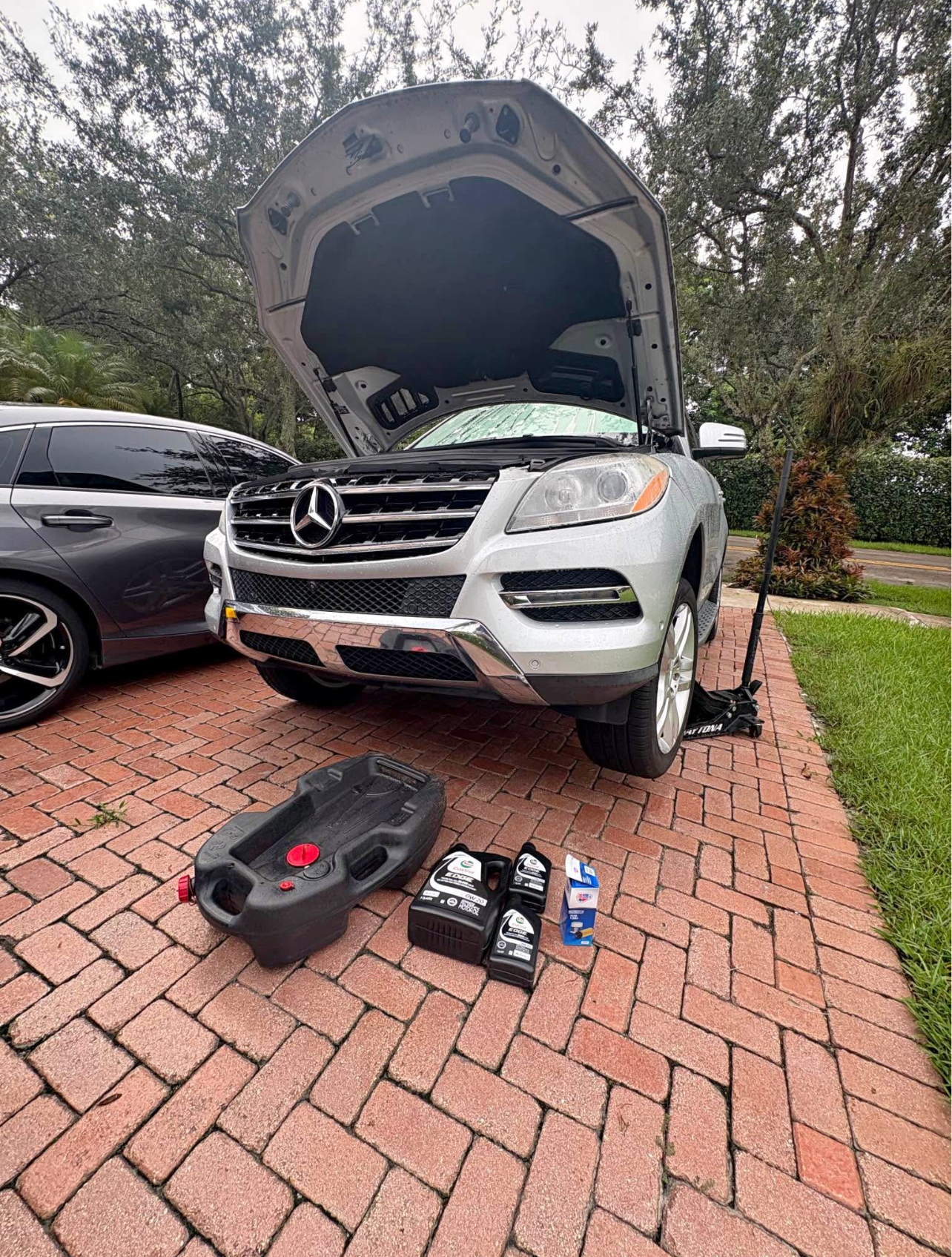 Mobile mechanic performing an oil change on a Mercedes SUV in the driveway
